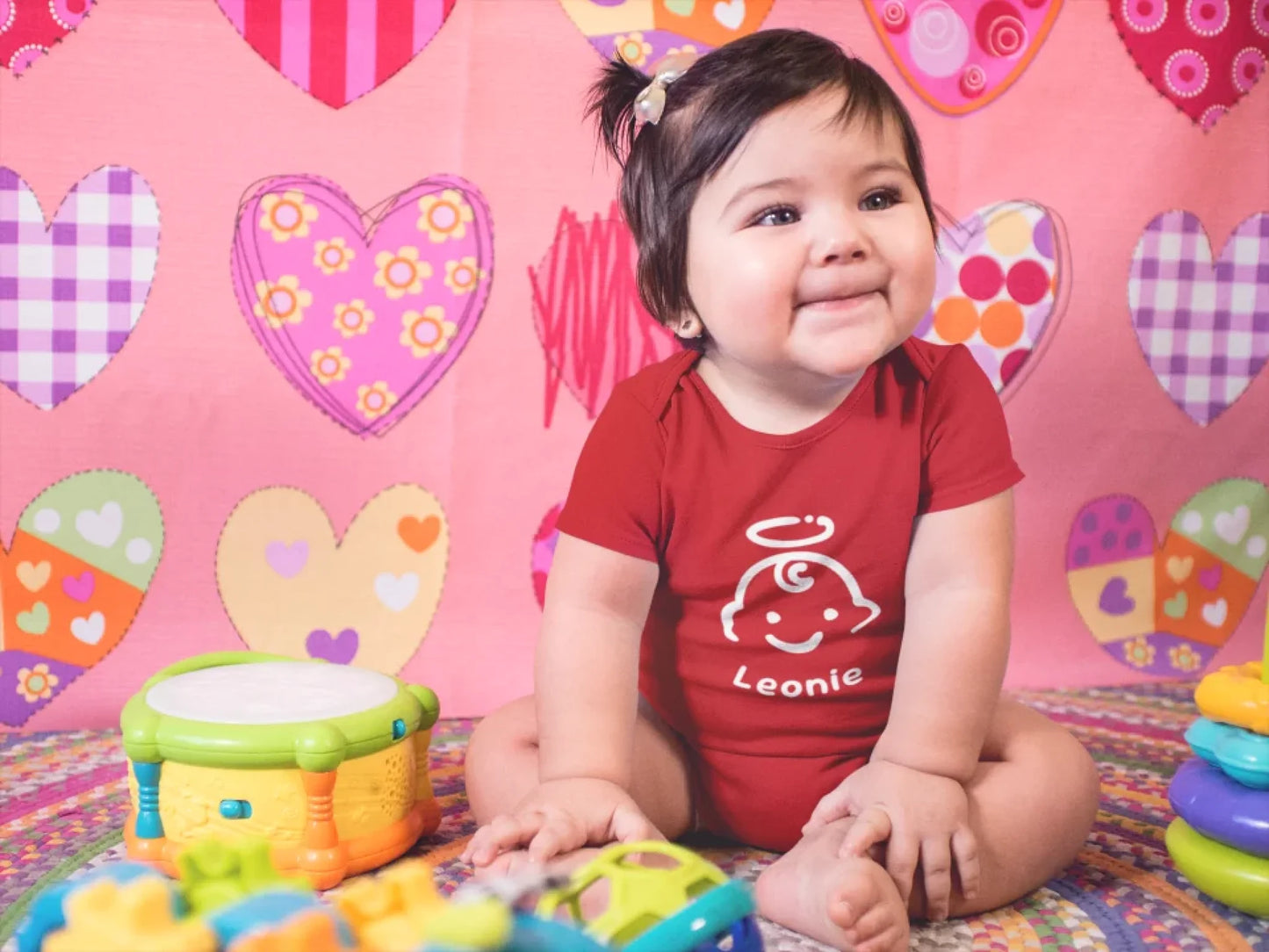 mockup-of-a-very-happy-baby-girl-sitting-down-on-her-playing-room-while-wearing-a-onesie-a14052